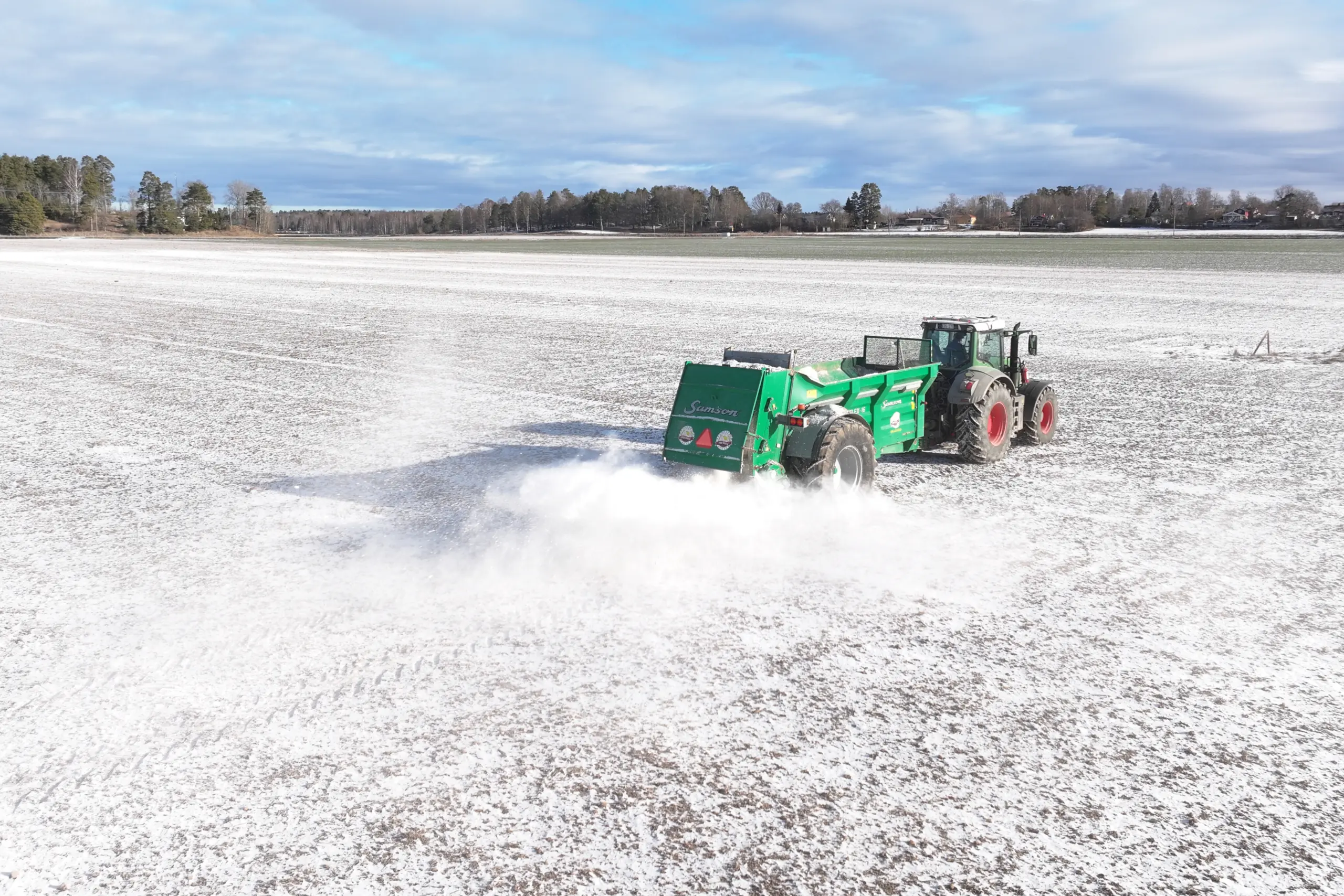 Vinterkalkning på snötäckt åker, traktor sprider kalk